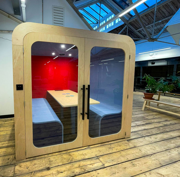 Dapapod acoustic meeting booth with deep red wool interior in a warehouse-style office