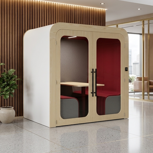 Modern office pod with red interior in a well-lit room with plants and furniture.