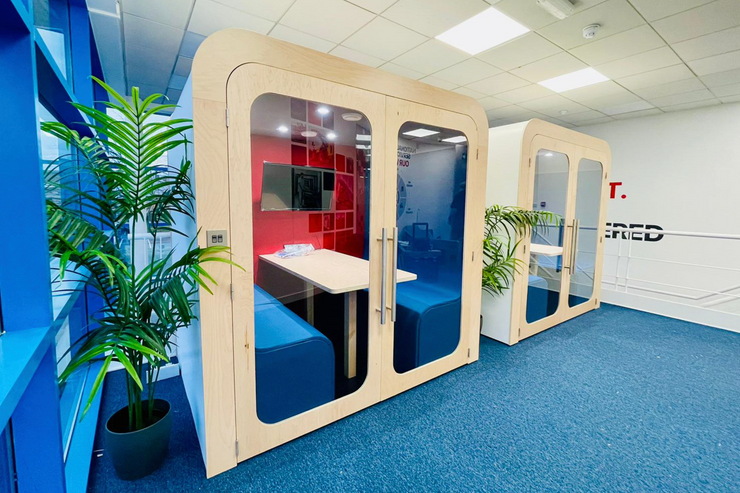 Two Dapapod four-person acoustic meeting booths with blue interiors in an open-plan office